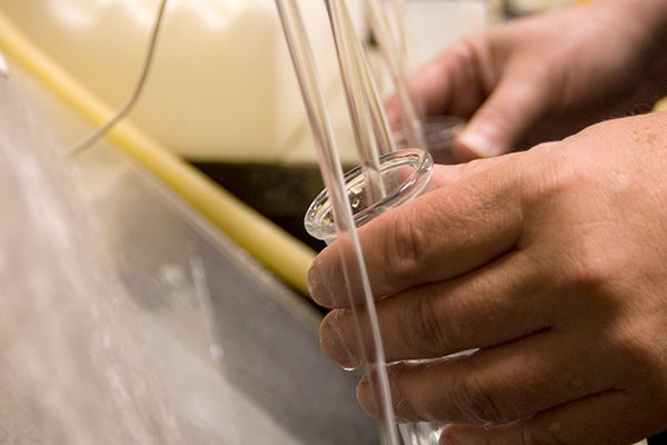 Close up of hands capturing water in a glass jar for testing.