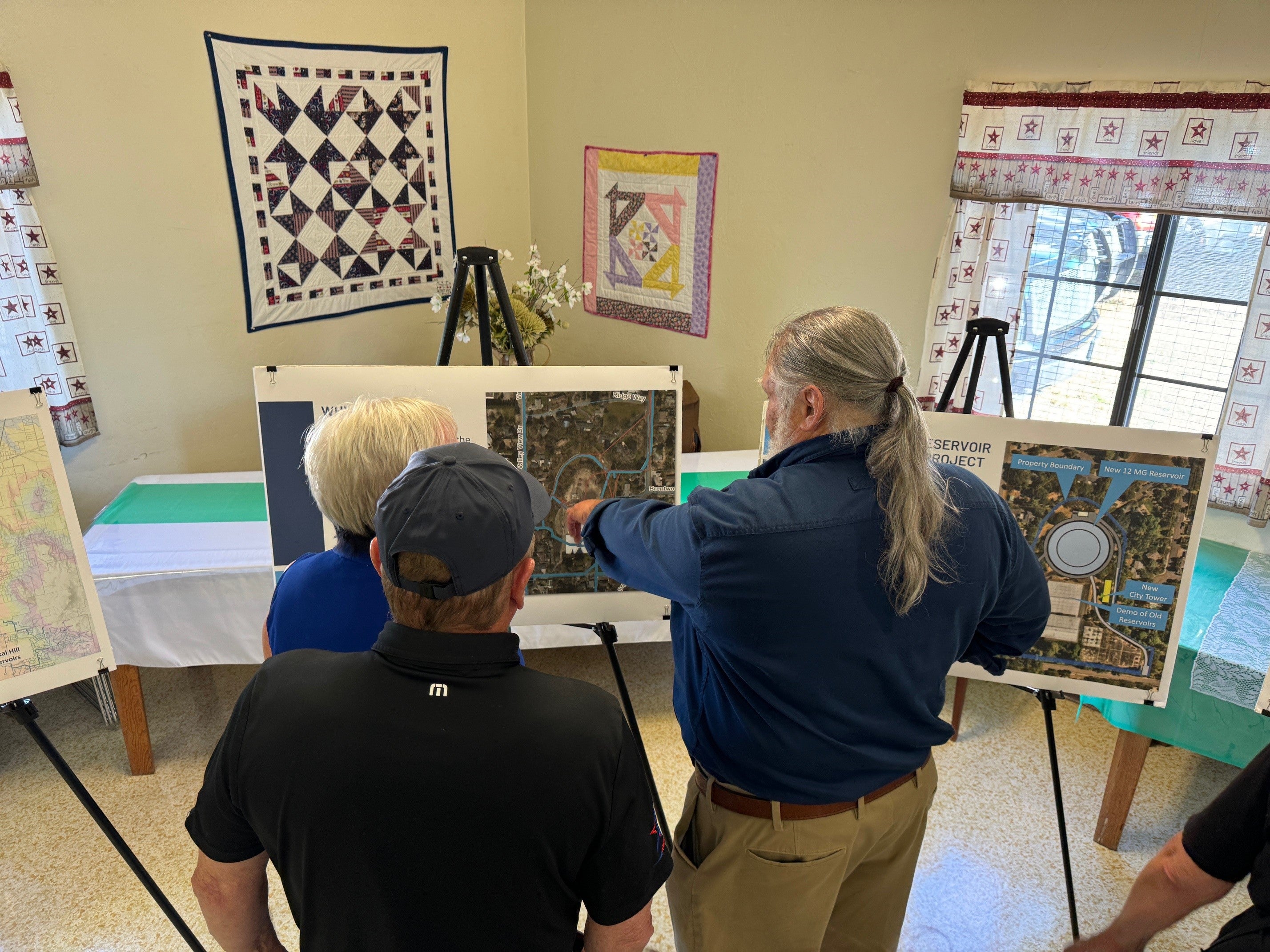 People point at map of reservoir project in a home covered in quilts.