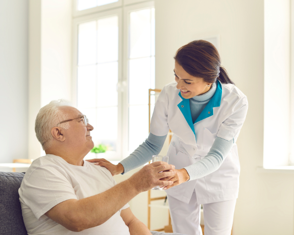 female care taker offers water to elderly man