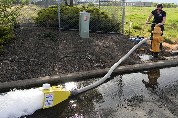person flushes out a fire hydrant using a pump.