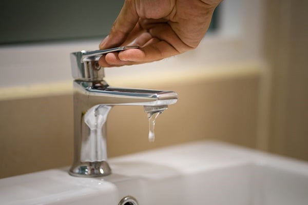 A hand turning off a leaky faucet