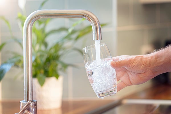 A hand holding a glass cup under a flowing water faucet.