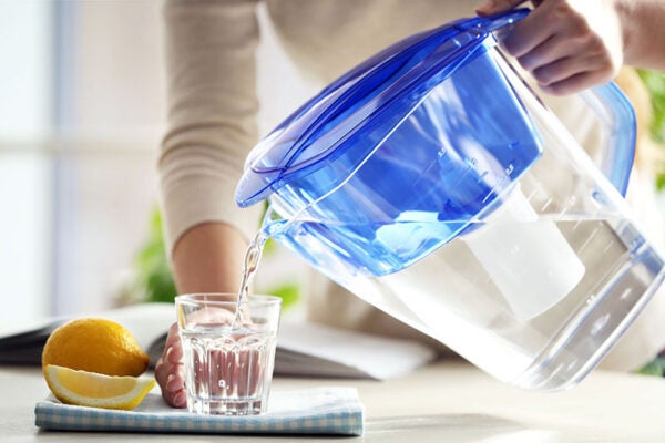 Woman pouring water from filter jug into glass in the kitchen
